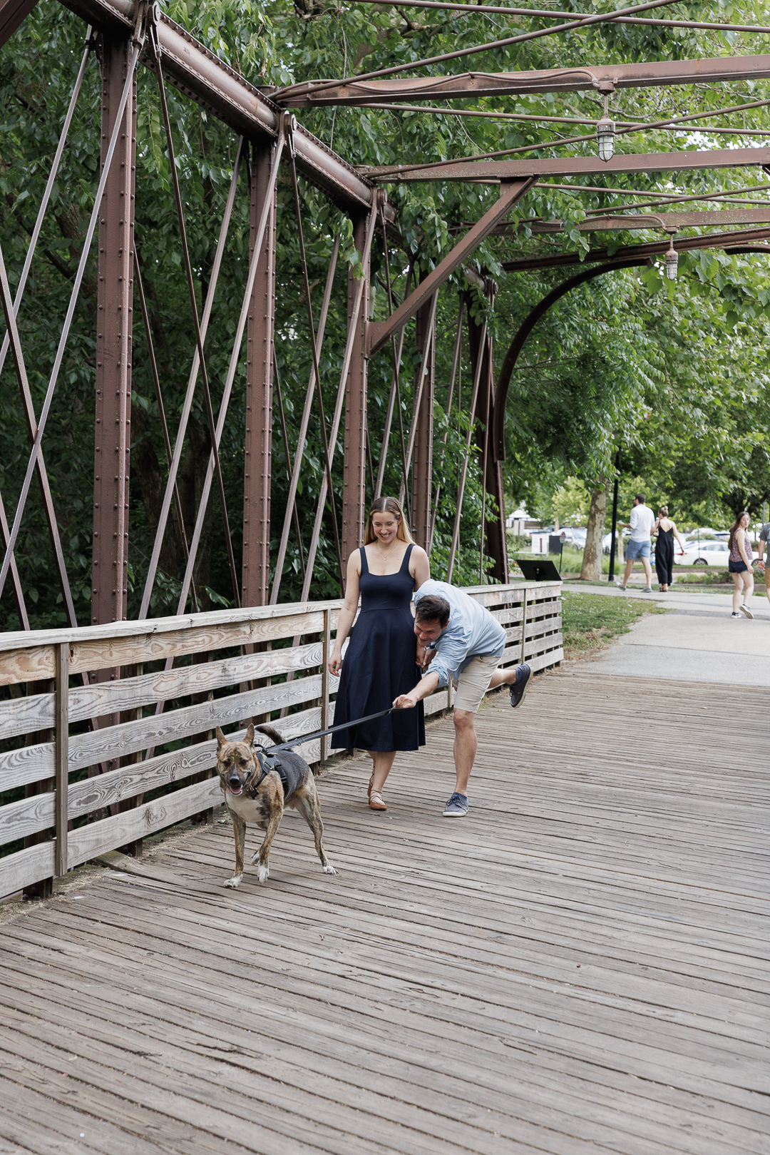 Bride-to-be Selah watches as Bryce tries to hold onto their dog's leash during a real engagement session photograpy moment