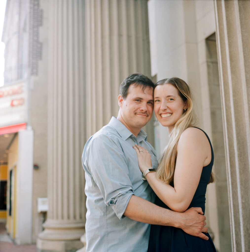 Couple embraces on sidewalk of Bridge Street, Phoenixville where they had their first date, during engagement session photography